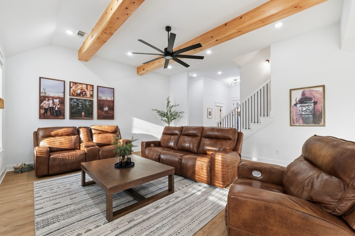 Bright living room with leather reclining sofas, wood ceiling beam, and curated wall art — real estate interior photography by Oakmont Visuals